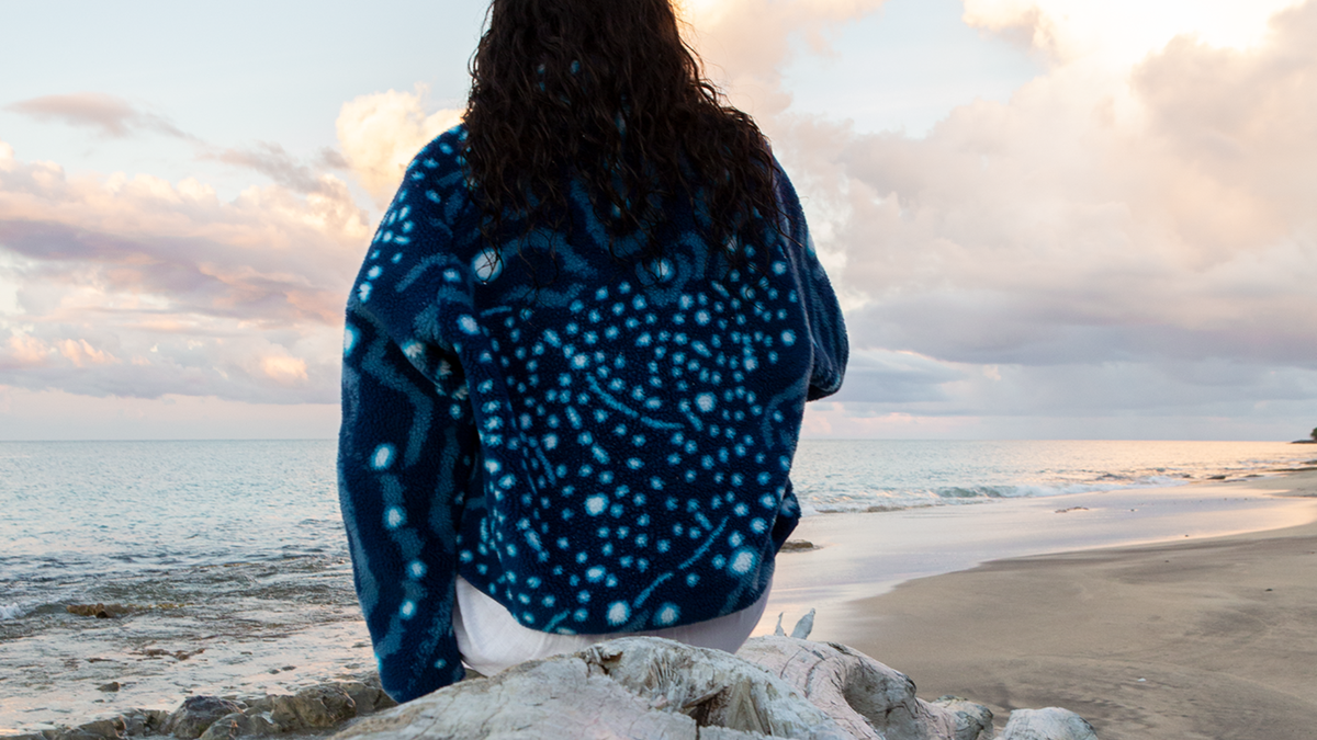 Model wearing an ocean-inspired fleece jacket on a beach, shown from front and back after swimming.