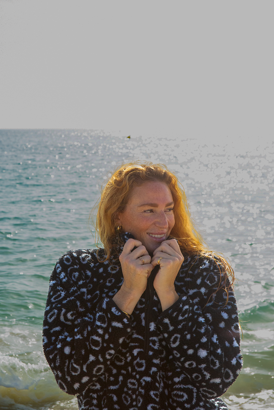 Eagle ray print black and white recycled womens fleece worn on the beach by a red haired woman.