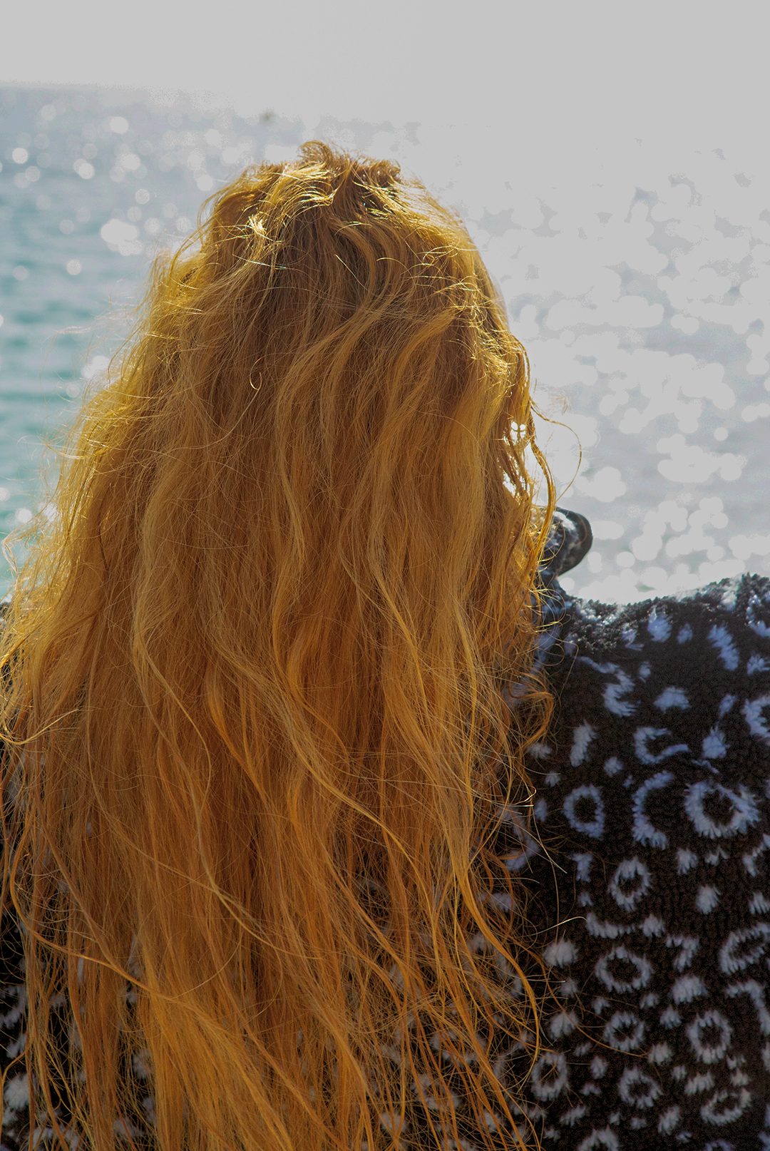 Eagle ray print black and white recycled womens fleece worn on the beach by a red haired woman.