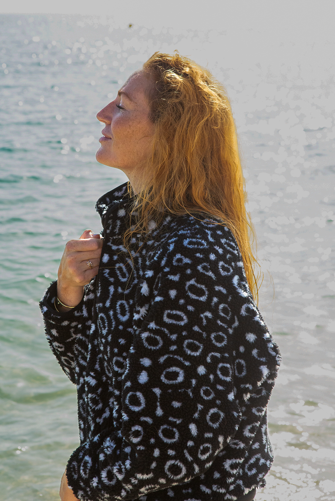 Eagle ray print black and white recycled womens fleece worn on the beach by a red haired woman.