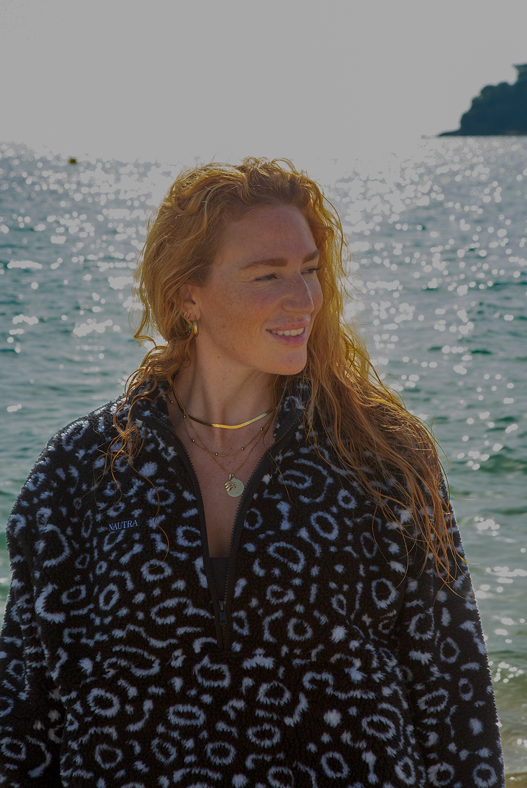 Eagle ray print black and white recycled womens fleece worn on the beach by a red haired woman.