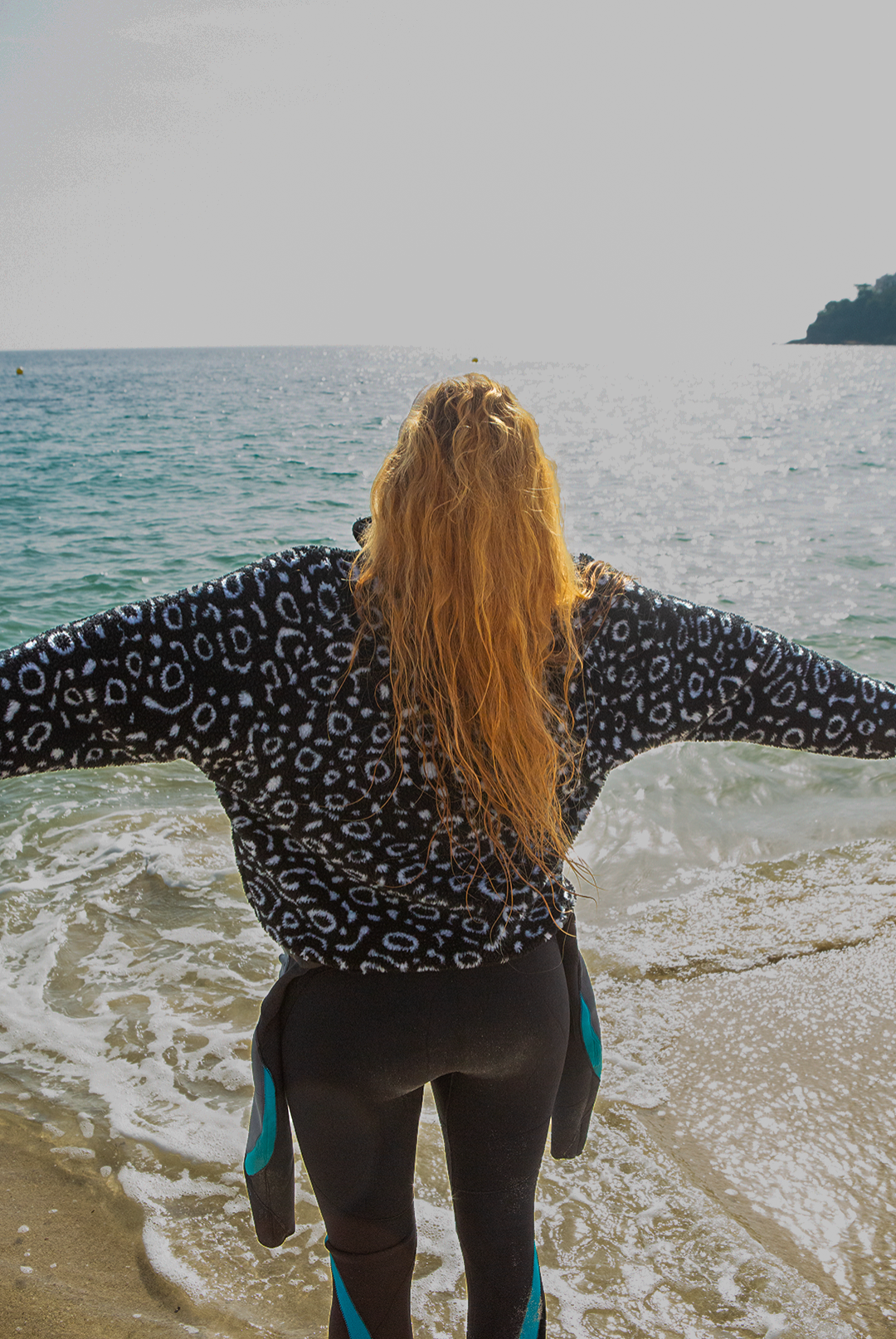 Eagle ray print black and white recycled womens fleece worn on the beach by a red haired woman.