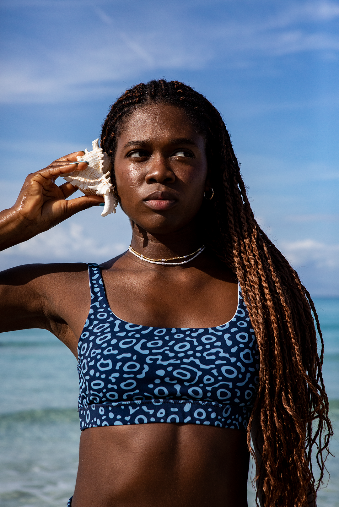  A woman wears NAUTRA’s Eagle Ray Bikini Top by the shore. This eco-friendly scoop neck sports bra is chlorine-resistant and built for adventure.