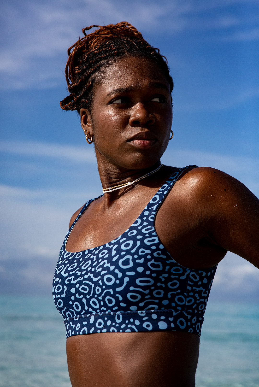 A woman wears NAUTRA’s Eagle Ray Bikini Top by the shore. This eco-friendly scoop neck sports bra is chlorine-resistant and built for adventure.