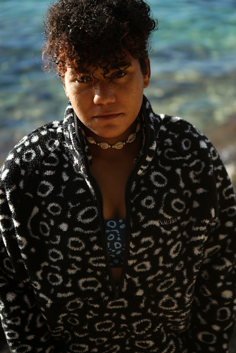 Close-up portrait of model wearing the NAUTRA Eagle Ray Fleece with ocean in soft focus behind.