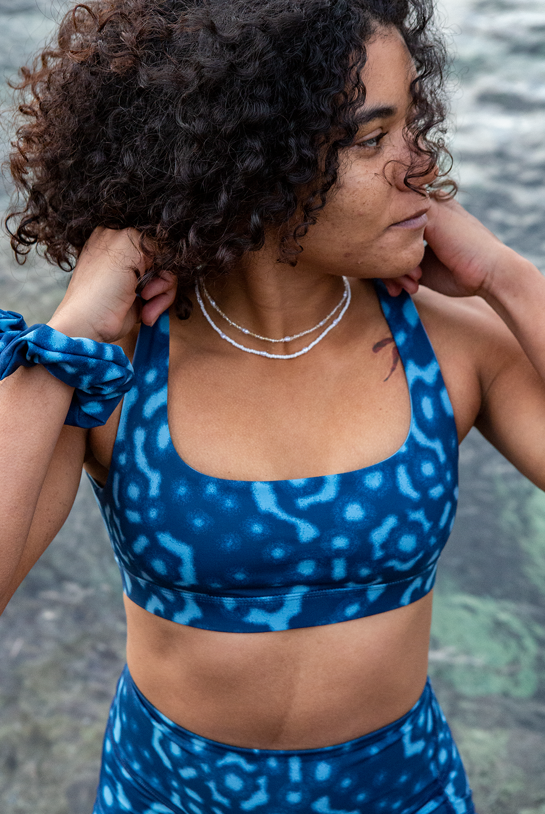 A woman wears NAUTRA’s Whale Shark Bikini Top on a rocky shore. This eco-friendly scoop neck sports bra is chlorine-resistant and made for land and sea.
