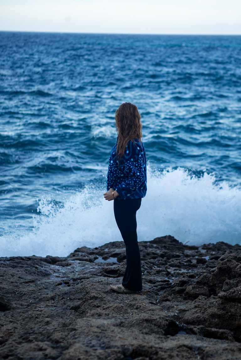 Side profile of woman in NAUTRA Whale Shark Fleece looking out at the sea, ocean spray in the background.