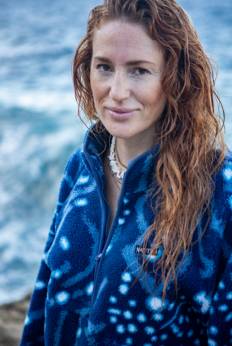 Woman wearing the NAUTRA Whale Shark Fleece made from recycled plastic bottles, standing by the ocean. Sustainable women’s fleece inspired by whale sharks.