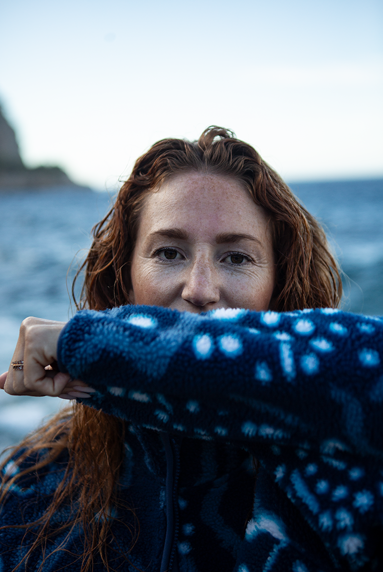 Model lifting arm to show sleeve detail of the Whale Shark Fleece, highlighting the blue and white ocean-inspired print.