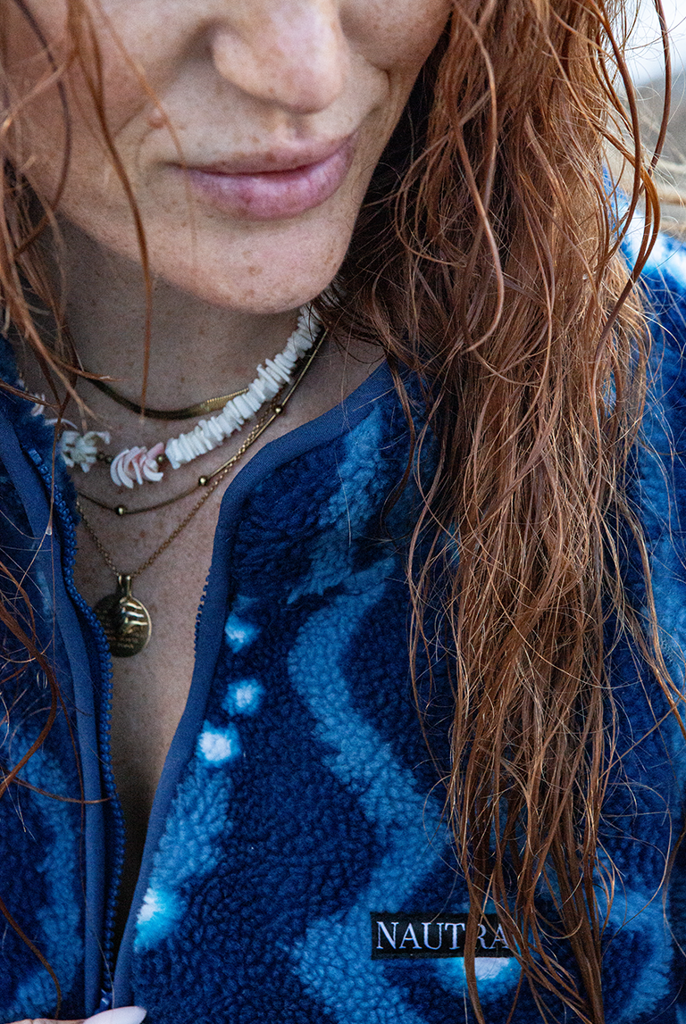 Detail of NAUTRA logo and zip on the Whale Shark Fleece with model wearing shell necklaces, wet hair from the sea.