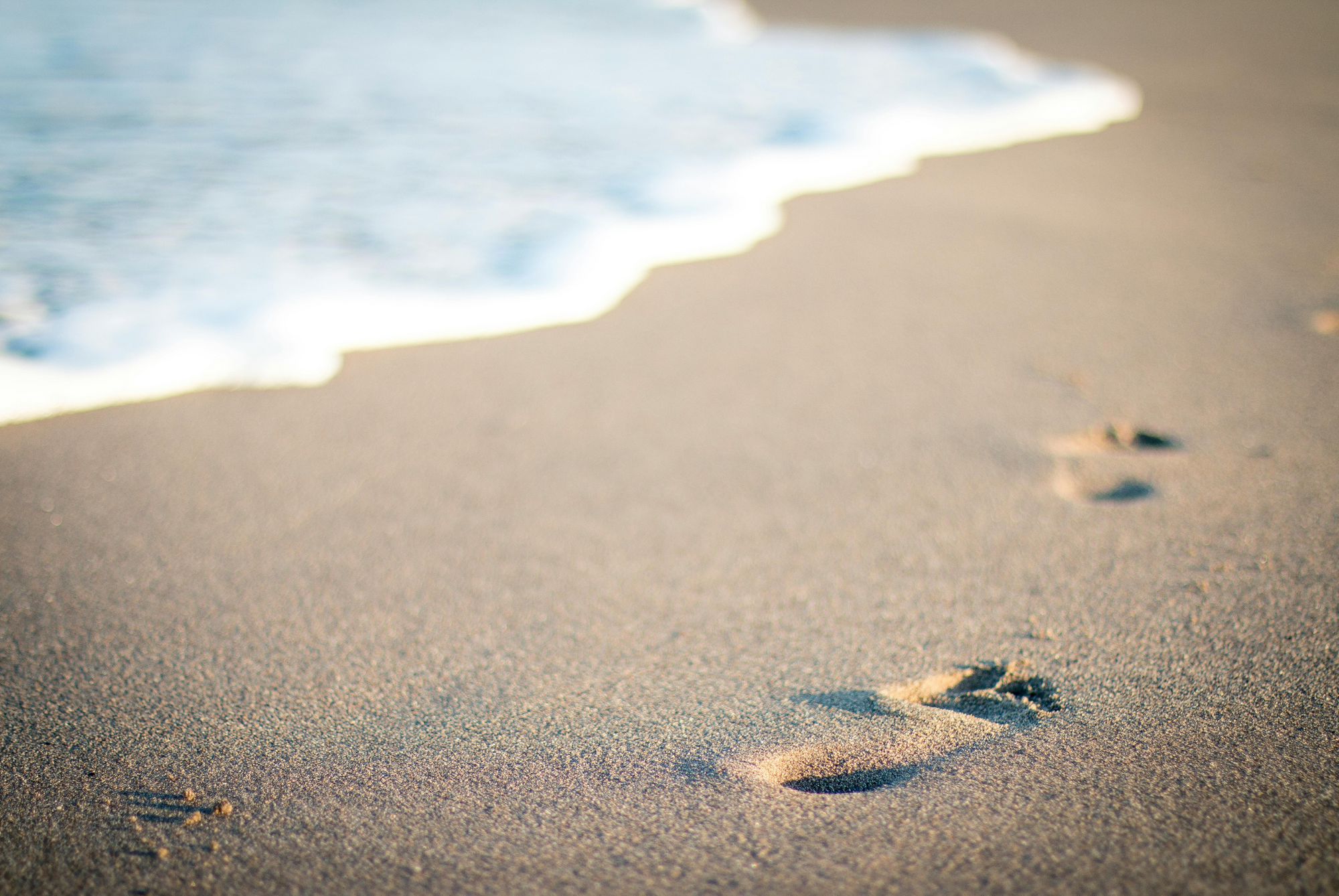 Footprints left in wet sand by the sea, symbolising NAUTRA’s origins and connection to life by the ocean.