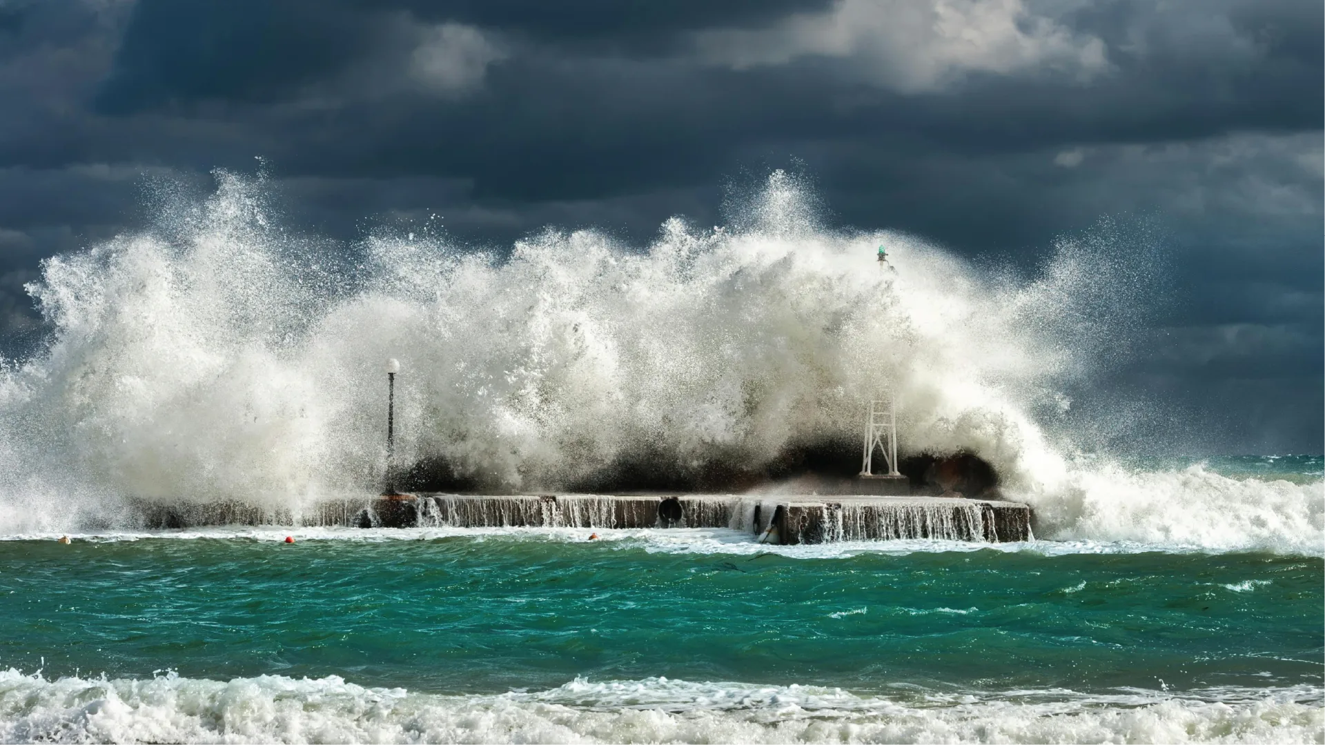 Powerful waves crashing against a pier under a dark, stormy sky.