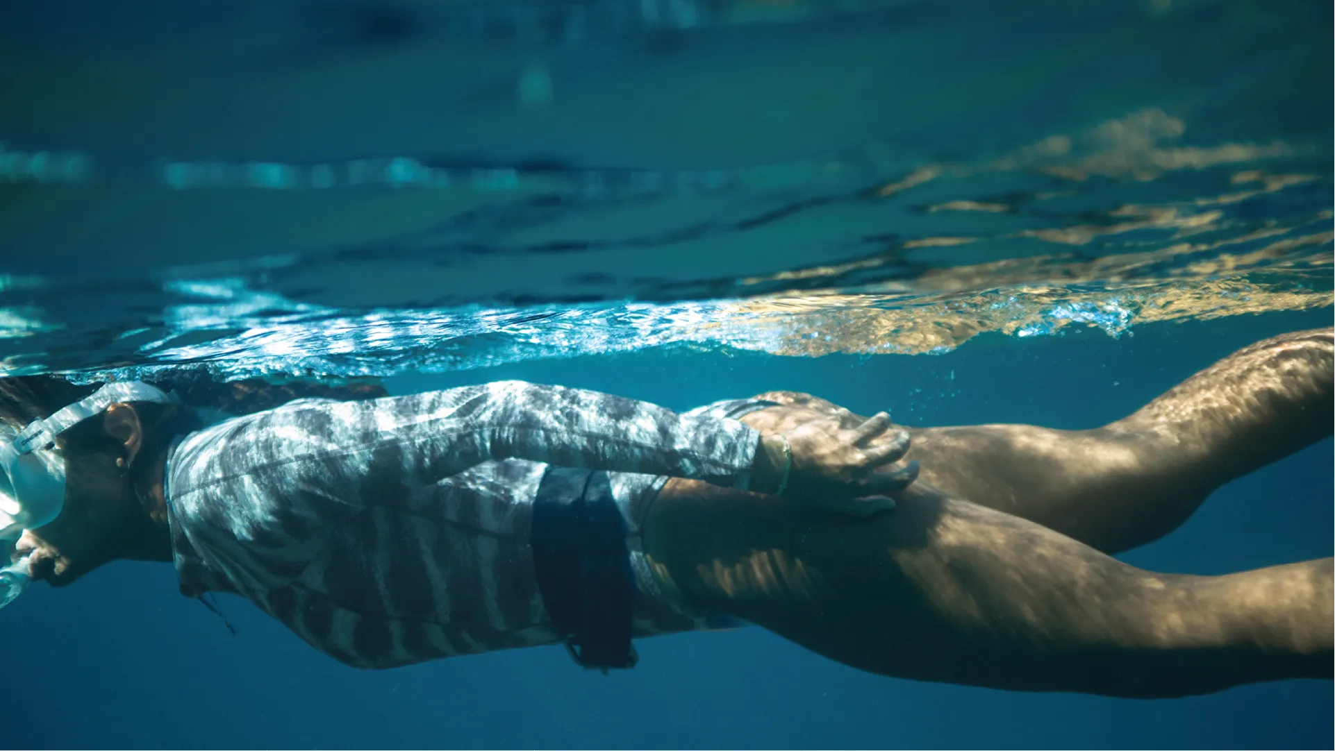 Woman wearing NAUTRA's tiger shark long sleeve swimsuit diving underwater.