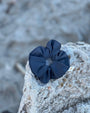 Minke grey scrunchie on a textured stone surface with a blurred natural background