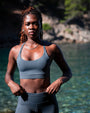 Grey recycled strappy sports bra bikini top inspired by the minke whale, worn by model by the sea, sustainable swimwear by NAUTRA.