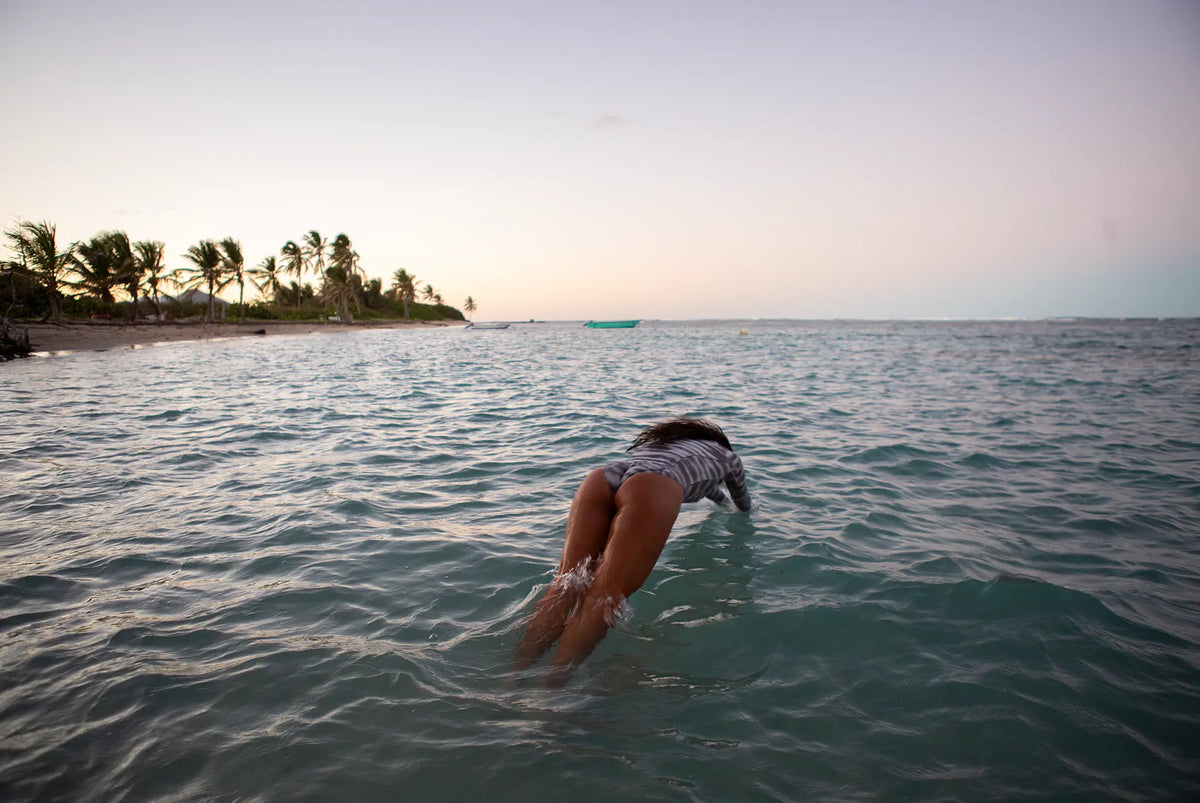 Model wearing NAUTRA's tiger shark swimsuit diving into the ocean with a tropical island in the background